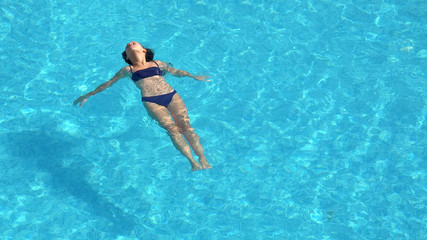 Young woman swimming in the crystal-clear pool laying on water surface