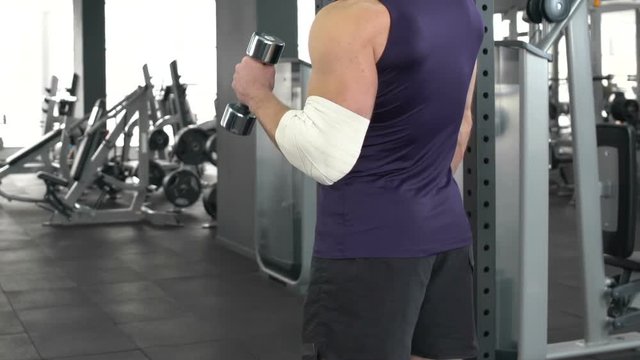 Sportsman with injured elbow slowly raising dumbbell, recovery, health problem