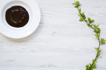 Panacotta dessert with chocolate in white plate on white wooden background decorated with blossoming cherry branch. Flat lay. Top view. From above. Copy space.