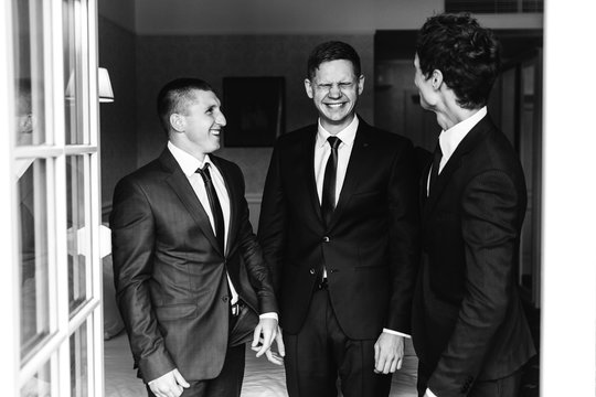 Three men in business suit stand before an open balcony and laugh