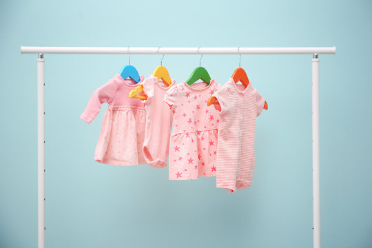 Baby clothes hanging on rack against color background