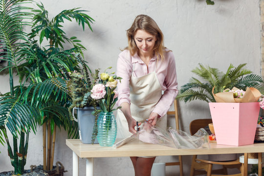 Photo of florist woman cutting film at table with flowers, paper