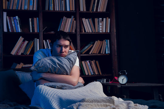 Photo of man with insomnia sitting in bed next to alarm clock