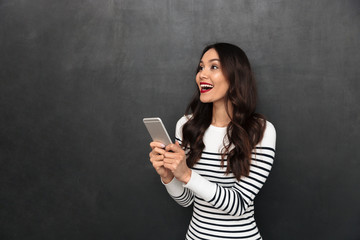 Surprised happy brunette woman in sweater holding smartphone