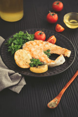 Grilled salmon with lemon and basil on dark background.