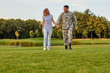 Fototapeta premium Soldier with girlfriend walking holding hands. Happy cheerful couple outdoor in the park.