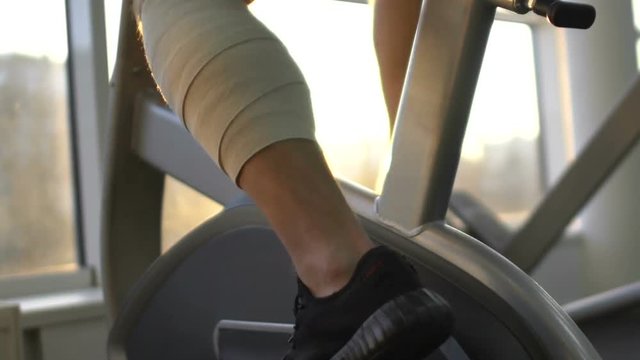 Man with injured leg riding stationary bike in morning sunlight, health recovery