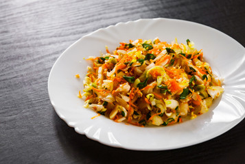 fresh vegetables salad with cabbage and carrot in a white plate on dark wooden table
