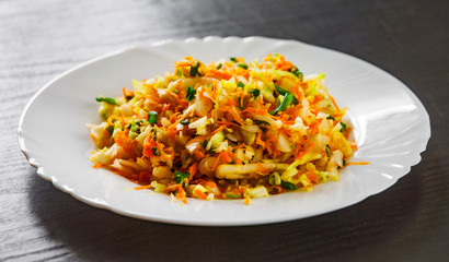 fresh vegetables salad with cabbage and carrot in a white plate on dark wooden table