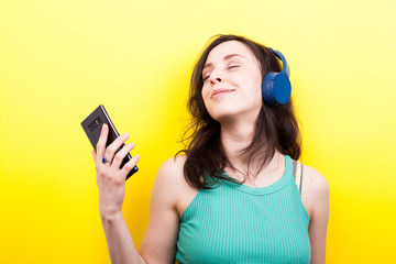 Smiling girl with a smartphone in hands listening to music on yellow background in studio