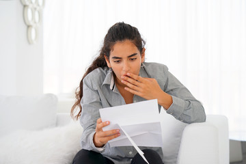 Woman reads negative news in a letter at home on the couch. The shaken business manager of the beauty girl received a notice of dismissal from the company, surprised. An agitated girl without joy.