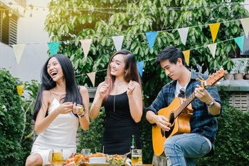 Group of friends having party in home garden.Happy young mates enjoying party playing guitar, singing and drinking beer eating food in garden.