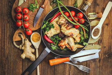 cooking fried chicken wings in a frying pan. spices and vegetables. old kitchen accessories. wooden background