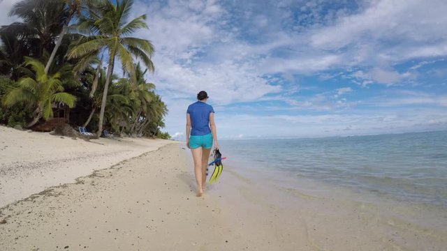 Young woman holds and walks with snorkel gear along Titikaveka lagoon in Rarotonga, Cook Islands. Real people. Copy space