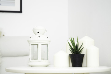 A white candle lamp and a small potted plant are placed on the table in the white bedroom.