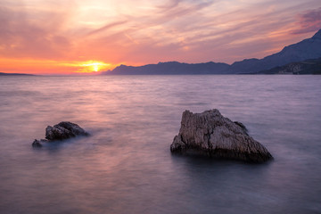 Fototapeta na wymiar Langzeitbelichtung - Farbenfroher Sonnenuntergang mit Felsen, Gebirge und Wolken am Meer I