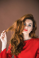 Beautiful young girl playing with hair isolated on brown background