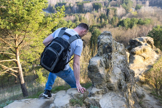 man with a rucksack climbs among rocks, stones