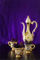 Still life with dates with goldenTraditional Arabic coffee set with dallah and mini cup. Dark background. Vertical photo.