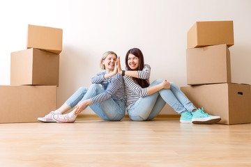 Photo of young blonde and brunette on floor among cardboard boxes