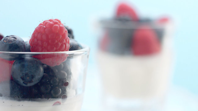 glasses with greek yogurt with berries Minimalism food on blue background. Panna cotta with strawberry raspberry, blueberry