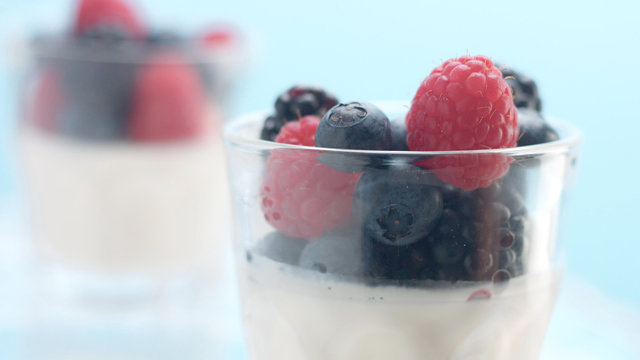glasses with greek yogurt with berries Minimalism food on blue background. Panna cotta with strawberry raspberry, blueberry