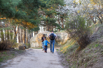 family, three, mom, dad, son are walking in the woods, people are driving along the path in the park in the spring