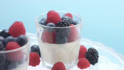 glasses with greek yogurt with berries Minimalism food on blue background. Panna cotta with strawberry raspberry, blueberry