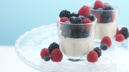 glasses with greek yogurt with berries Minimalism food on blue background. Panna cotta with strawberry raspberry, blueberry