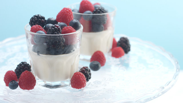 glasses with greek yogurt with berries Minimalism food on blue background. Panna cotta with strawberry raspberry, blueberry