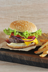 Hamburger with minced beef patties with tomato, salad, bacon, cheese, sauce and onions. Next to the hamburger is French fries. Close-up. Light background. Vertical orientation of the frame.