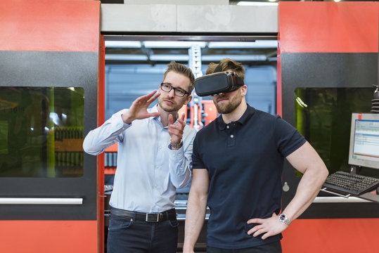 Man explaining machine to colleague wearing VR glasses in factory