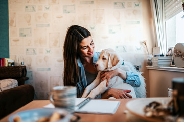 Woman sitting by the table in her apartment with cute puppy.