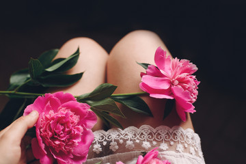 lovely pink peonies on legs of boho girl in white bohemian dress, top view. space for text. stylish hipster woman sitting with beautiful flowers in morning room. atmospheric sensual moment