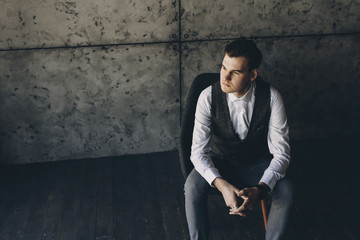 Upper view of a young confident executive sitting in char in his office and looking away seriously against a grey wall.