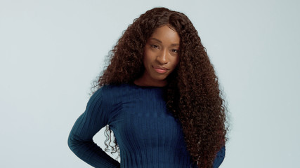 Beauty black mixed race african american woman with long curly hair and perfect smile looking at camera and smiling on blue