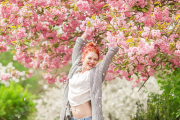 Beautiful young woman with red hair having fun standing in cherry blossom tree, springtime garden mood