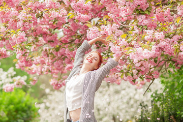 Beautiful young woman with red hair having fun standing in cherry blossom tree, springtime garden mood