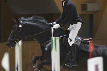 Young rider on black horse galloping at show jumping competition