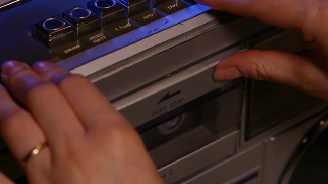 Woman hands place a compact music cassette tape in old retro player - closeup, camera tilt up