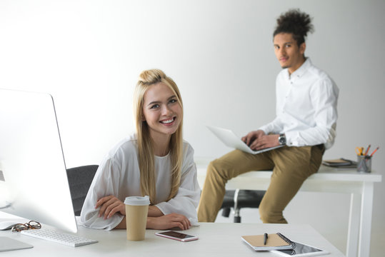 beautiful young businesswoman smiling at camera dand male colleague using laptop behind