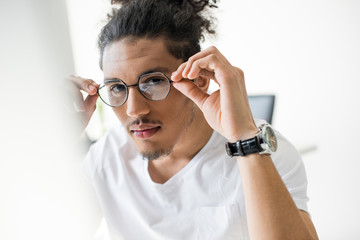 handsome young african american man wearing eyeglasses and looking at camera at workplace
