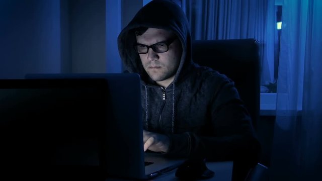 Footage of young man wearing hoodie and eyeglasses working at computer. Concept of programist or hacker