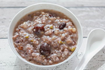 Eight Treasure Congee on traditional chinese festive porridge, mixed from eight ingredients: red beans, lotus seeds, peanuts, dates, pine nuts, lily, almond and walnut on white wooden table, top view