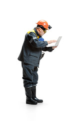 The studio shot of pensive senior bearded male miner standing in profile view at the camera with laptop on a white background.