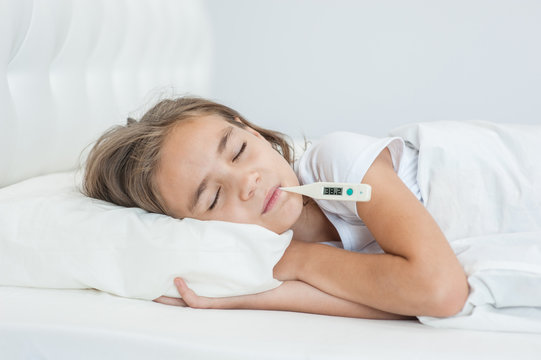 sick girl sleeping on the bed with a thermometer in mouth