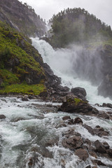 Waterfall on the mountain river in the rocky gorge overgrown with the wood, Norway