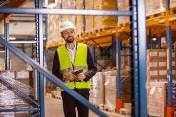 In the storehouse. Positive joyful man using a scanner device while checking the boxes in the storehouse