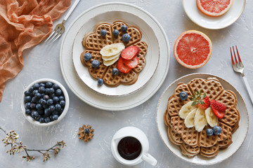 Pieces of homemade waffle cake with banana and blueberries on the plates on gray background