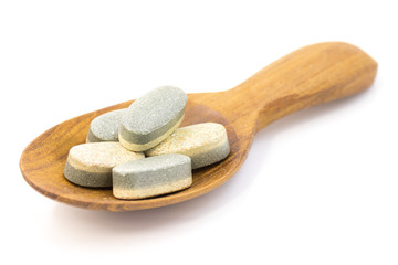 Muti vitamin tablets on wooden spoon isolated on white background, herbal pill with two color